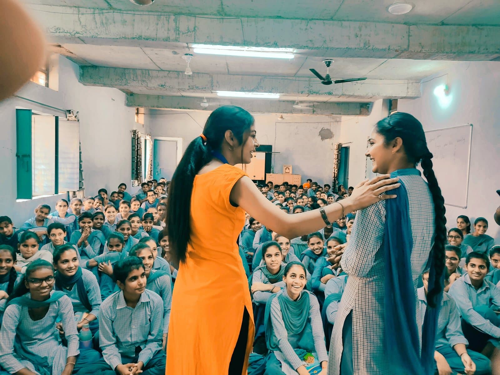 Anju Verma speaking with a student in front of a hall packed with schoolgirls, all smiling