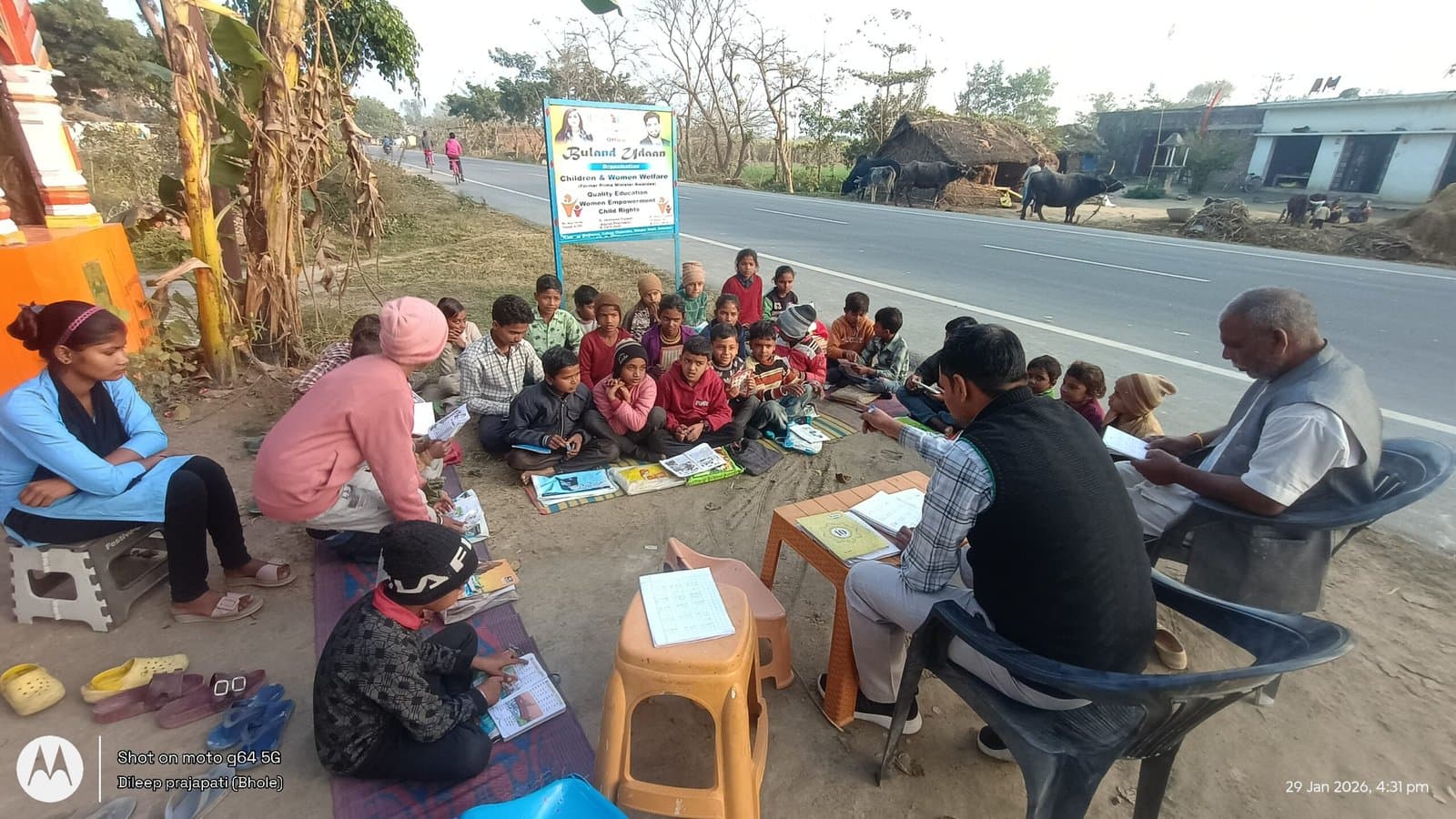 Children and volunteers seated on mats at the roadside Pathshala in Bahraich, with the Buland Udaan signboard behind them