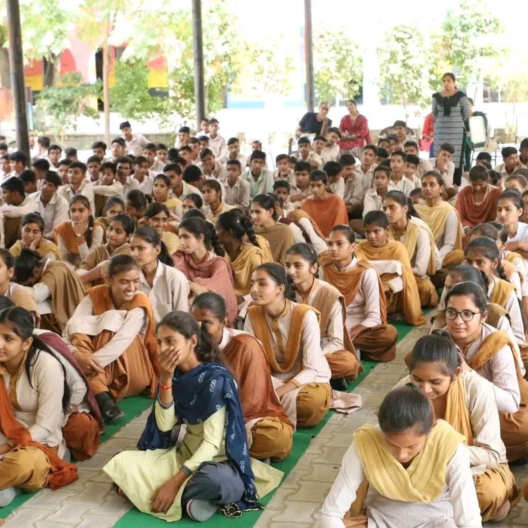 Hundreds of school students seated on the ground during an outdoor Buland Udaan assembly