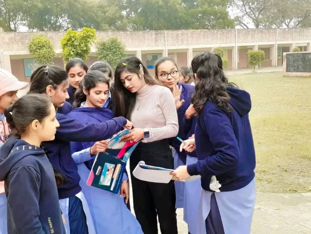 A Buland Udaan team member handing out programme material to a group of schoolgirls in navy uniforms in a school courtyard