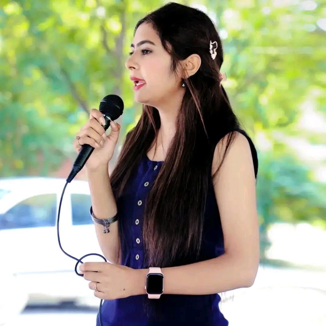 Anju Verma addressing an audience with a microphone at an outdoor event